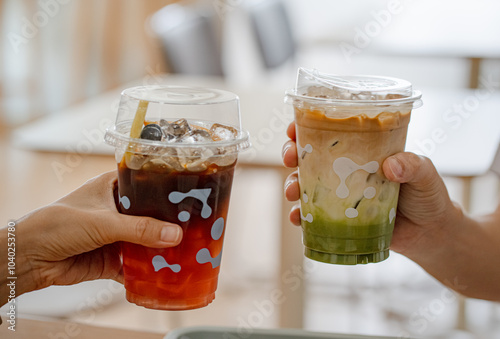 Hands of teenage girl and boy holding glass of ice tea with lemon and ice coffee with matcha green tea together at cafe.