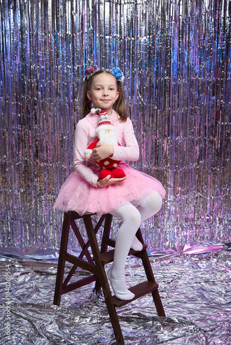 A little girl is sitting in the living room near the Christmas tree with Santa Claus in her hands, New Year's magic