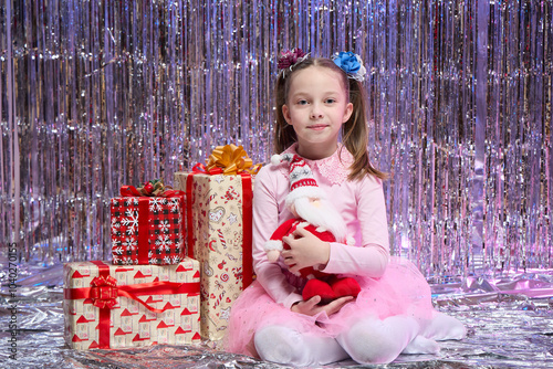 A little girl is sitting in the living room near the Christmas tree with Santa Claus in her hands, New Year's magic