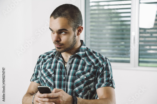 Young man looking aside while texting on smartphone