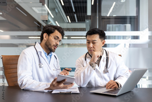 Doctors engaged in discussion over patient diagnosis in an office setting, utilizing tablet and laptop. Emphasizing teamwork, collaboration, healthcare, and technology.