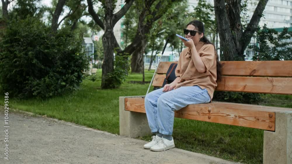 Positive girl with visual impairment communicating with friend in voice chat while sitting on bench in park Positive girl with visual impairment communicating with friend in voice chat while sitting on bench in park