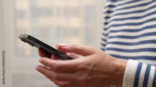A close-up of hands holding a smartphone at home or work. Woman using smartphone, scrolling and reading social media internet, typing text or shopping online