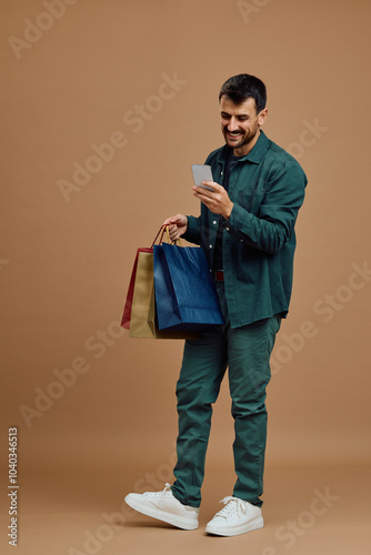 Studio shot of happy man with shopping bags using cell phone.