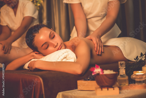 Caucasian couple customer enjoying relaxing anti-stress spa massage and pampering with beauty skin recreation leisure in warm candle lighting ambient salon spa at luxury resort or hotel. Quiescent