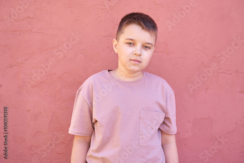 Casual portrait of a young boy in pink t-shirt against a textured pink wall background.