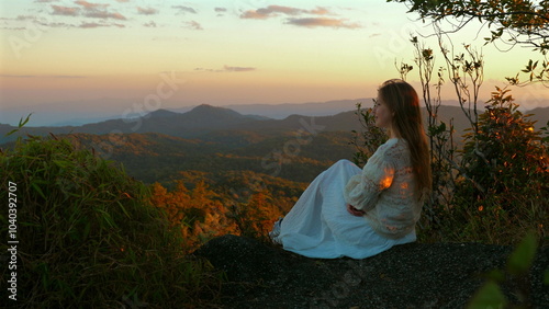 Wallpaper Mural Young woman in white dress sitting on mountaintop at sunset, enjoying scenic view of rolling hills and distant mountains. Tranquility and Nature. Torontodigital.ca