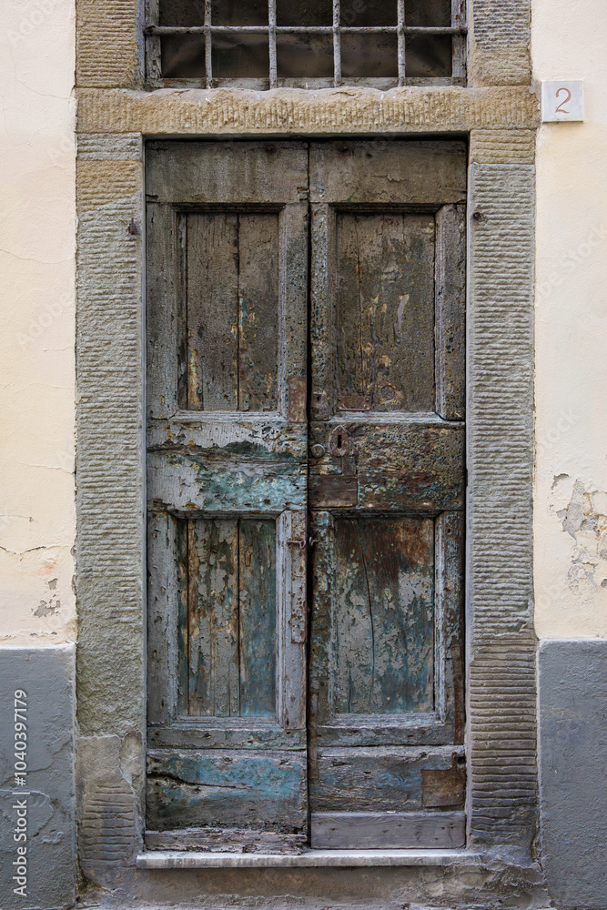 Fototapeta premium Shabby old double door entrance of stone building in Europe. Vintage wooden doorway of ancient stone house. Simple grey brown wood door. Architecture in Italy.
