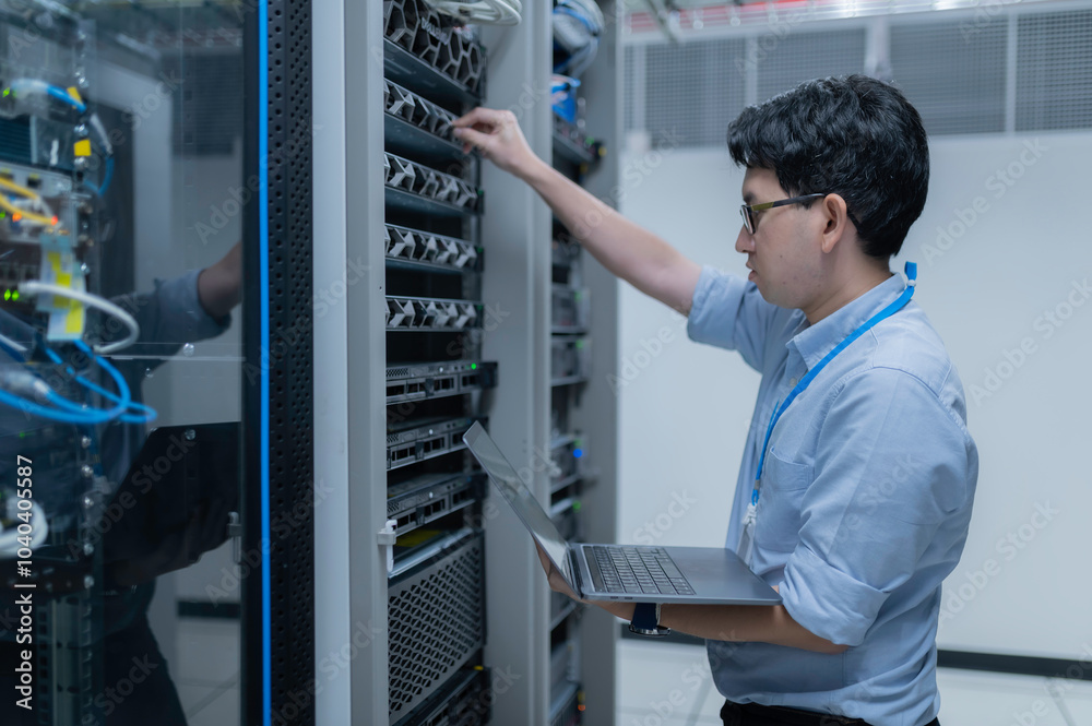 Fototapeta premium Computer engineer is setting up network in server room,Systems Maintenance Technician,Male engineer working in server room at modern data center