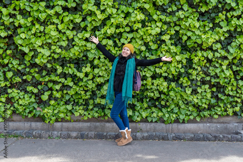 oyful Latino woman in her 30s with arms wide open celebrating life in front of a vibrant green plant wall photo