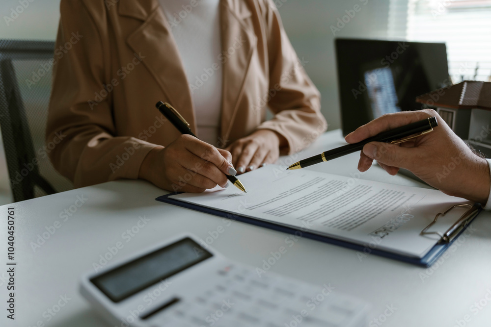 Fototapeta premium Businesswoman is signing a contract while being assisted by a realtor who is pointing at the document