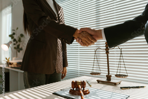 Two businesspeople are shaking hands in a law office with a scale and a gavel on the table photo