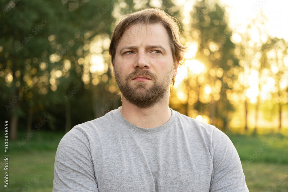 Portrait of handsome young man in gray t-shirt outdoors. Male with long hair and beard feel happy, calm and serious on Green nature sunset background. Man looking away into distance. Diversity People Portrait of handsome young man in gray t-shirt outdoors. Male with long hair and beard feel happy, calm and serious on Green nature sunset background. Man looking away into distance. Diversity People