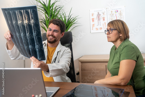 Health consultant explaining diagnosis to woman patient in clinic office medium shot. Doctor showing MRI scans of spine to beautiful middle-aged female patient. Doctor showing MRI to his patient. 