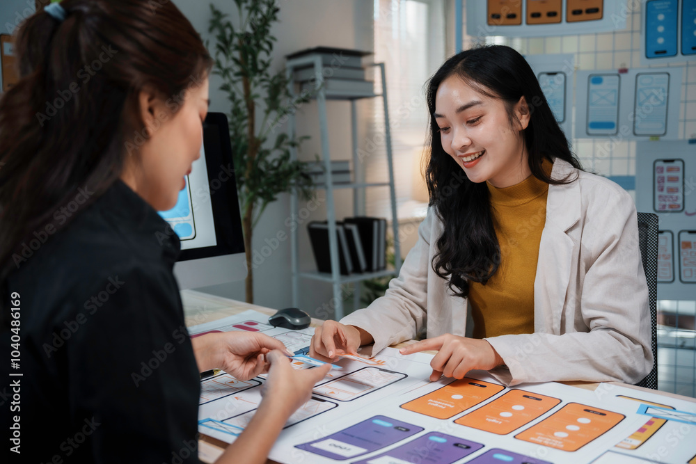 Fototapeta premium Two female uiux designers are discussing over a new mobile application interface wireframe design in the office