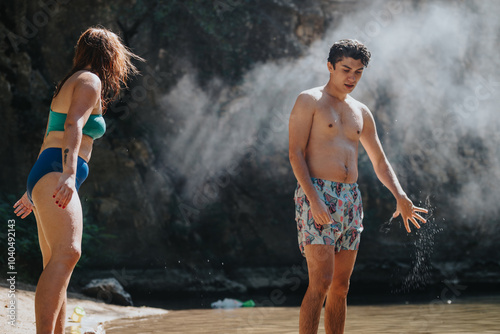 Two young adults in swimsuits enjoying a sunny day by a natural water spot. Leisure and relaxation in a serene outdoor setting with mist and sunlight creating a calm atmosphere. photo