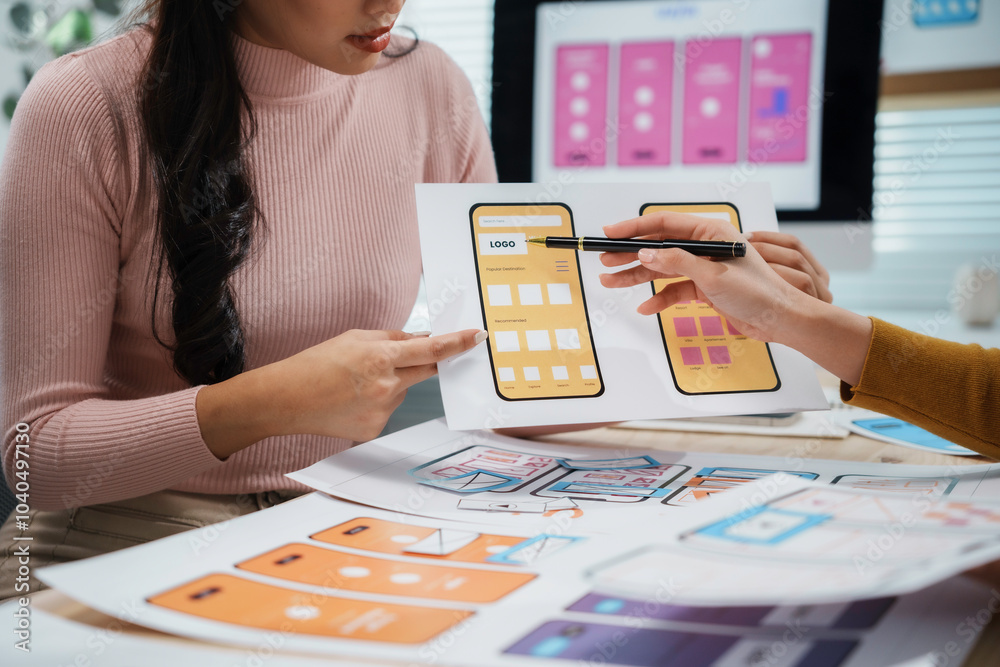 Two female uiux designers are working together in the office, discussing over new mobile application interface wireframe design