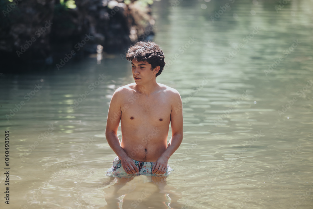 A young man stands waist-deep in a serene pond, enjoying a relaxing swim surrounded by nature. The sunny setting provides a peaceful atmosphere. A young man stands waist-deep in a serene pond, enjoying a relaxing swim surrounded by nature. The sunny setting provides a peaceful atmosphere.