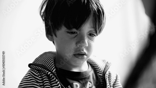 Black and white closeup of a young boy tearfully reflecting after crying, head slightly bowed as he processes emotions in a quiet, intimate moment indoors photo