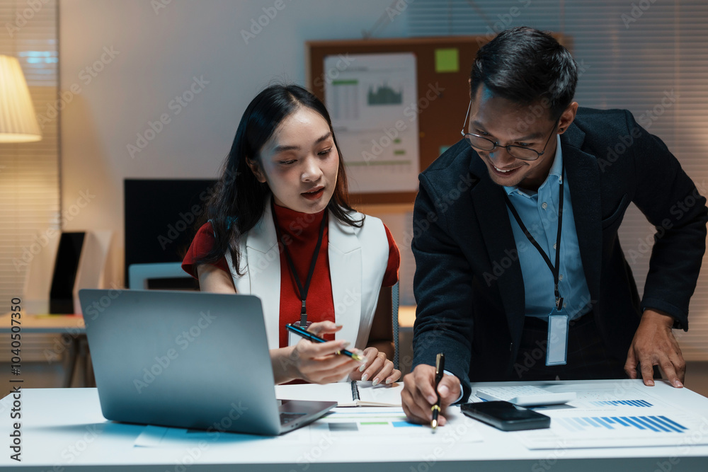 Two asian business people working late in the office are discussing strategy and reviewing financial reports Two asian business people working late in the office are discussing strategy and reviewing financial reports