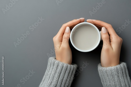 Cozy hands holding a warm cup of coffee on a soft gray background in a comfor...