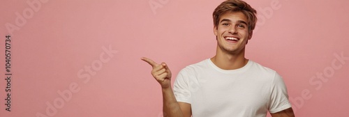Young man smiling enthusiastically while pointing upwards against a plain bac...