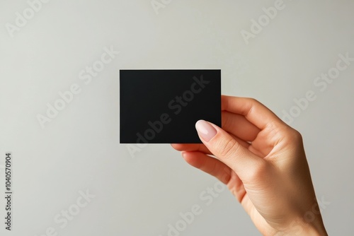 A person holding a blank black card against a plain background during dayligh...