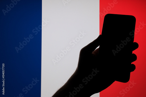 Silhouette of a person holding a smartphone in front of the flag of France photo