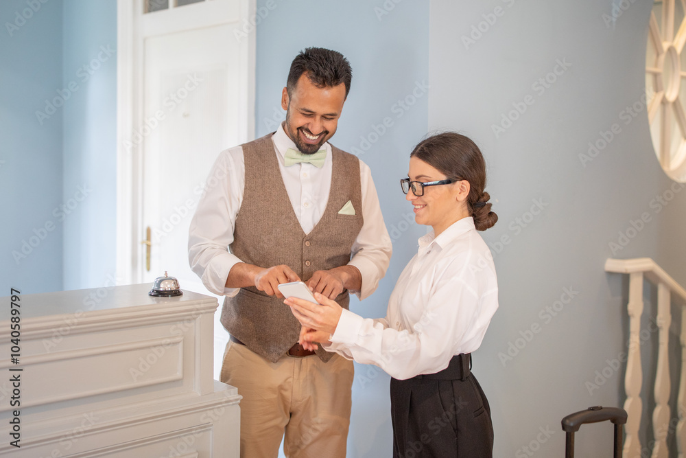 Obraz premium A smiling hotel receptionist assists a guest with their check-in process at an inviting boutique hotel during the day, showcasing a warm hospitality experience.