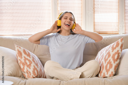 Smiling young woman in headphones sitting on sofa at home photo