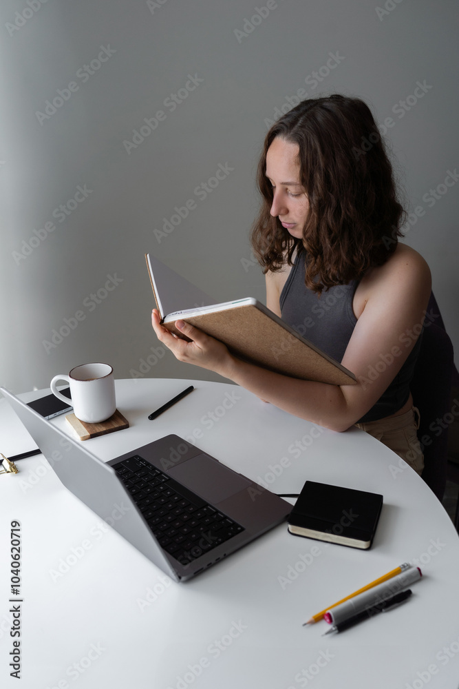 Focused woman reading from a notebook while working at home office desk Focused woman reading from a notebook while working at home office desk
