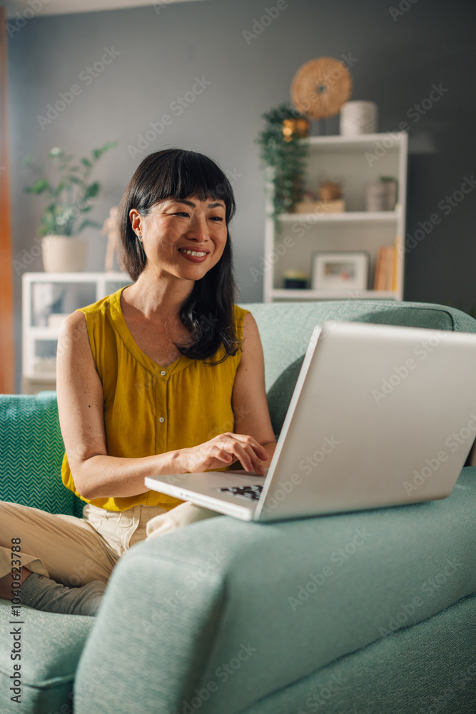 Focused asian woman typing on a laptop while sitting on a comfy couch. Focused asian woman typing on a laptop while sitting on a comfy couch.