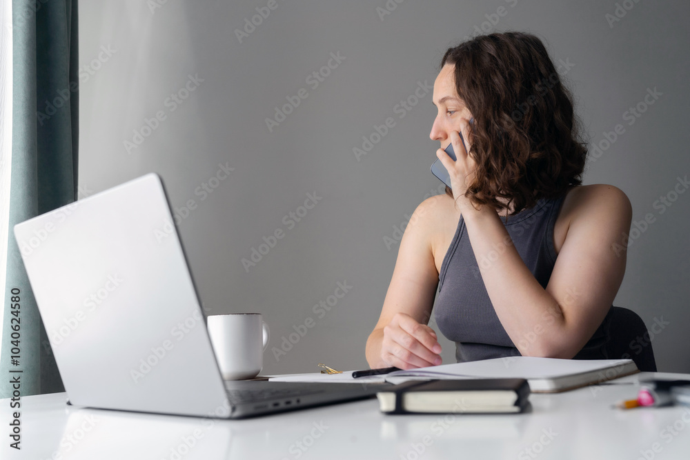 Woman managing work calls while sitting at home with laptop and notebook Woman managing work calls while sitting at home with laptop and notebook