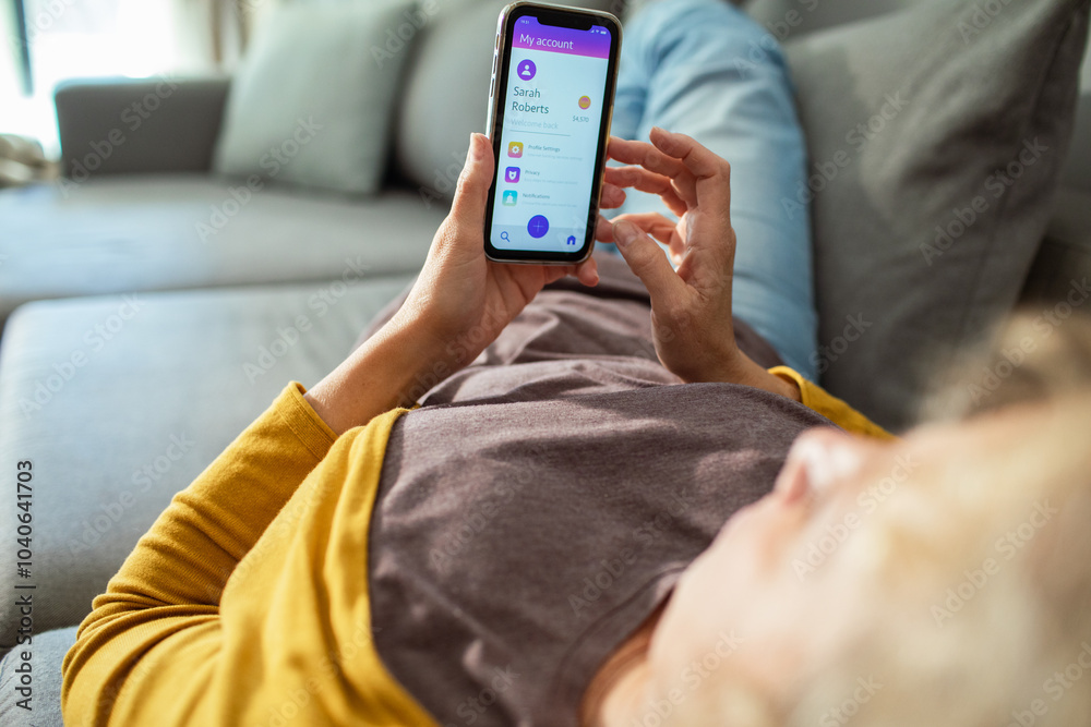 Senior woman managing online account on smartphone while relaxing on couch Senior woman managing online account on smartphone while relaxing on couch