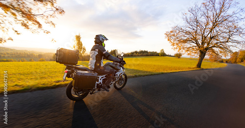 Driver riding motorcycle on empty road during sunset, autumn mountains