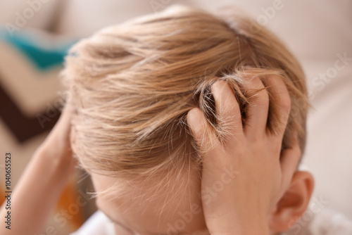 Little boy with pediculosis scratching his head at home, closeup photo