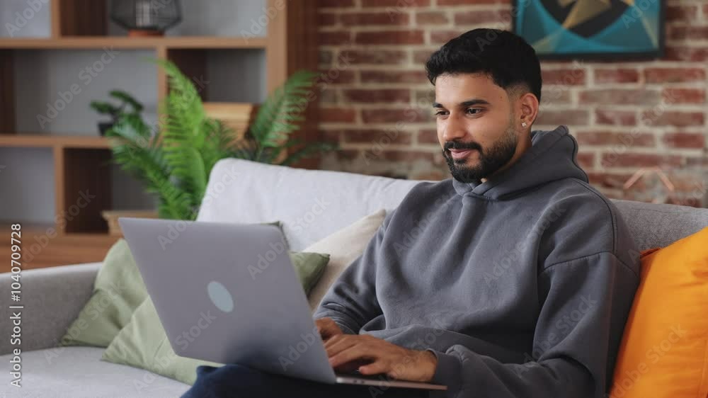 Overjoyed dark haired man holding computer on laps and cheering with victory gesture in renovated apartment. Excited male receiving email with food news and celebrating receiving approval. Overjoyed dark haired man holding computer on laps and cheering with victory gesture in renovated apartment. Excited male receiving email with food news and celebrating receiving approval.