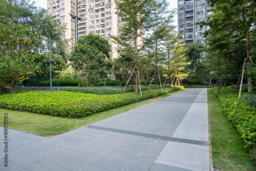 Modern Residential Complex Garden with Wide Paved Walkway and Manicured Landscapes with Mixed Vegetation, Including Ground Cover Plants and Tree-Lined Pathways in communal outdoor space of apartments photo