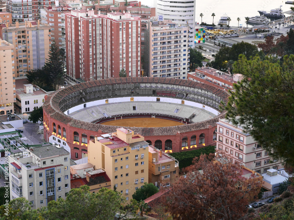 Aerial view of La Malagueta bullring in Malaga, Spain, surrounded by residential buildings and trees. The iconic circular arena stands out in the urban landscape, showcasing historic architecture