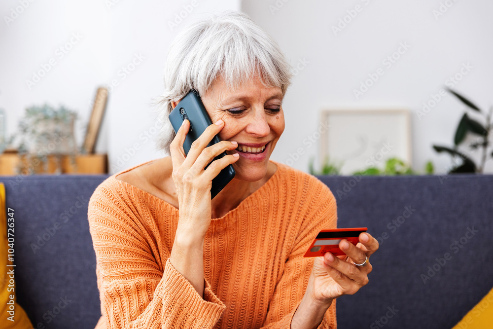 Fototapeta premium Senior woman making online shopping using credit card and talking on phone. Online payment and banking concept.