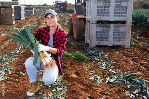 Happy smiling girl farmer posing on plantation of organic leek on spring day, holding freshly harvested vegetables.. photo