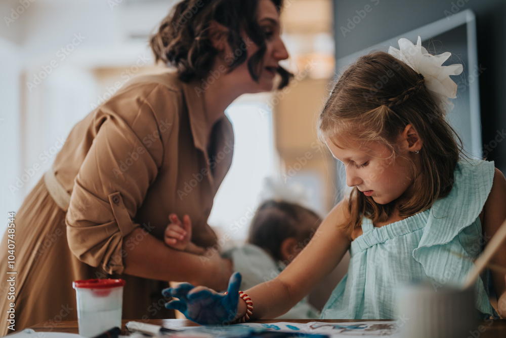 Fototapeta premium Mother helps her daughters during a fun and creative painting session at home, fostering creativity and bonding through art.
