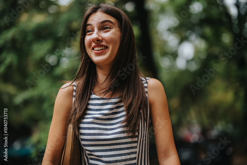 Bilde på lerret A joyful woman with long hair wearing a striped dress smiles warmly in a lush, green outdoor setting