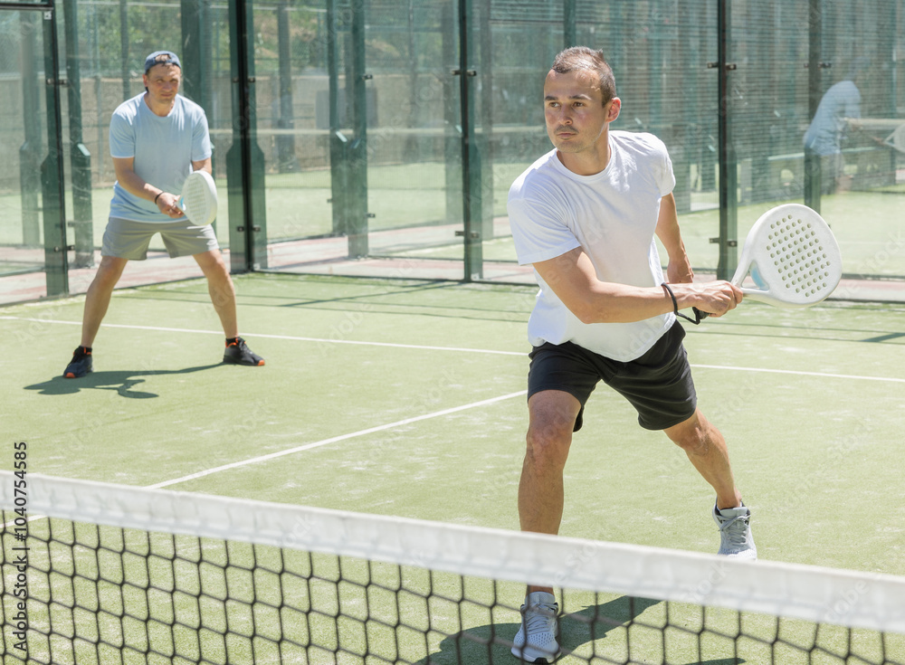Obraz premium Four men practice playing padel on an outdoor tennis court