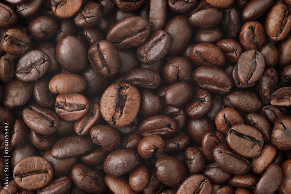 Obraz premium A close-up photograph of roasted coffee beans. The beans are dark brown, with visible texture and slight variations in size and shape. Glossy surface of the beans, indicating their freshness. 
