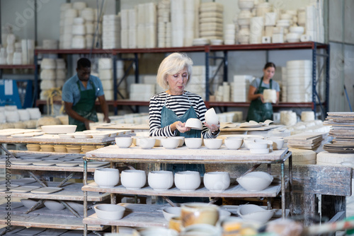 Mature female craftswoman checking quality of pottery in pottery factory photo