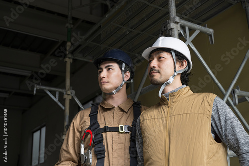 Serious and earnest expression of two gung-ho workers looking up from their work with safety belt harnesses for steeplejacks and outdoor work,copy space
