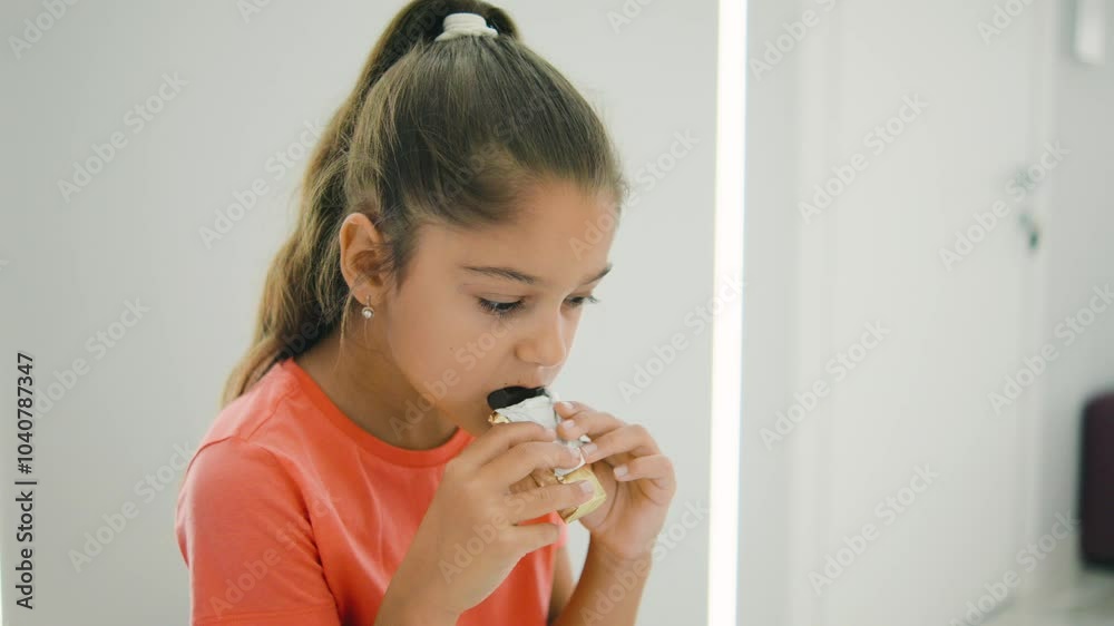 A young girl delightfully savoring a tasty snack in a bright and modern indoor space, surrounded by vibrant and colorful furniture decorations A young girl delightfully savoring a tasty snack in a bright and modern indoor space, surrounded by vibrant and colorful furniture decorations