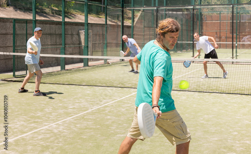 Two adult men doubles playing against two men in padel tennis on court photo