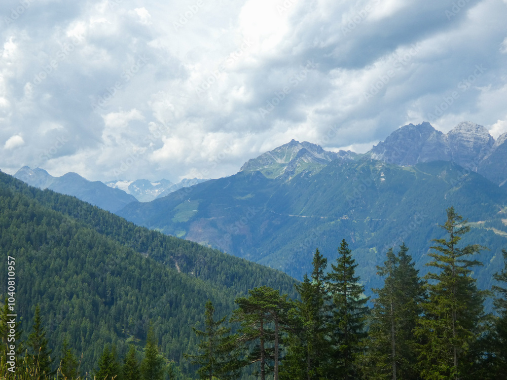 The Stubai Valley showcases the striking peaks of the Austrian Alps beneath a dramatic sky. Tall pine trees enhance the view, highlighting the natural landscape of the Tyrol region The Stubai Valley showcases the striking peaks of the Austrian Alps beneath a dramatic sky. Tall pine trees enhance the view, highlighting the natural landscape of the Tyrol region